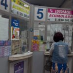 a imagem mostra uma mulher em um a lotérica. De fundo, a banca com anúncios divulgando os prêmios.